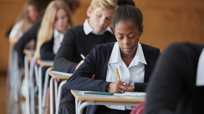 Teenage Students In Uniform Sitting Examination In School Hall