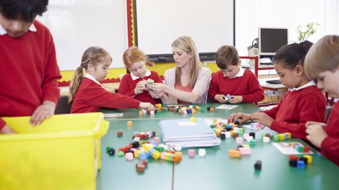 Primary School Pupils And Teacher Working With Coloured Blocks
