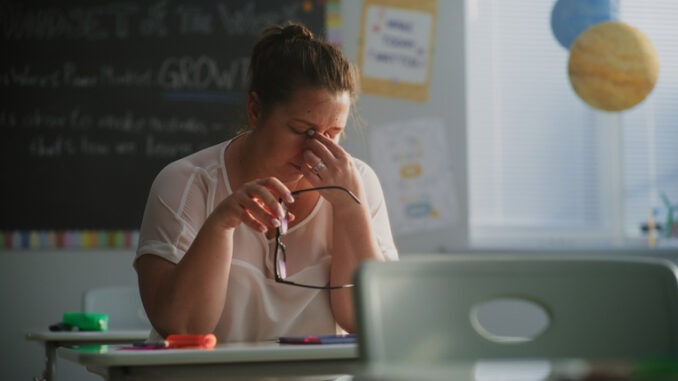Tired Female Teacher Sitting Alone at the Desk in Empty Classroom, Relaxing After Class. Woman Feeling Stress, Burnout and Mental Exhaustion in Educational Environment, Working in Elementary School.