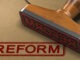 3D illustration of a rubber stamp with the word reform stamped on kraft paper envelope.
