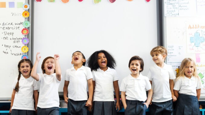 Group of diverse children students smiling in a classroom. Kids standing, laughing, and having fun in front of white board classroom. Classroom setting with students enjoying. Students enjoying class
