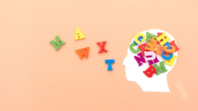 Conceptual Image of Human Head Silhouette Overflowing with Colorful Alphabet Letters on Peach Background