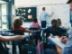 Male Trainee Teacher Being Observed Teaching In Classroom By Supervisor
