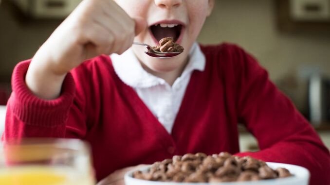 Close Up Of Girl Wearing School Uniform Eating Bowl Of Sugary Breakfast Cereal In Kitchen