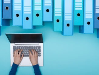 Organized archive with ring binders and woman searching for files in the database using a laptop, top view