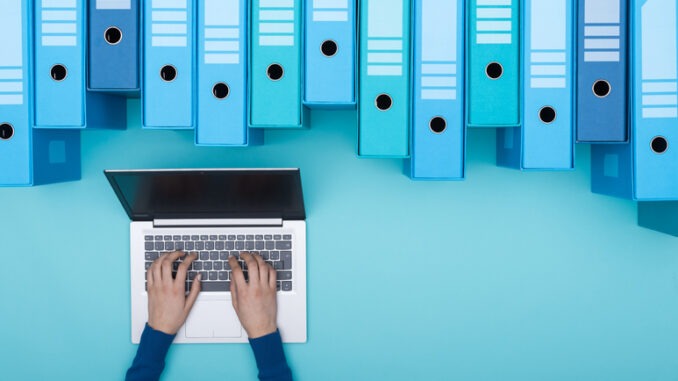 Organized archive with ring binders and woman searching for files in the database using a laptop, top view