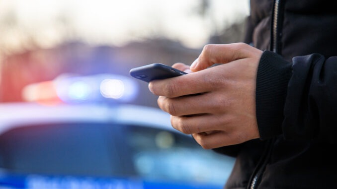 man holding phone with police car in street