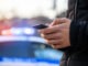 man holding phone with police car in street