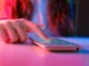 Use of mobile phone in trendy neon lights. Creative vivid color of ultraviolet red and blue. Hands of Teen Girl scrolling up photos Close-up at dark neon room. App for sale in shop. Social media. 4K