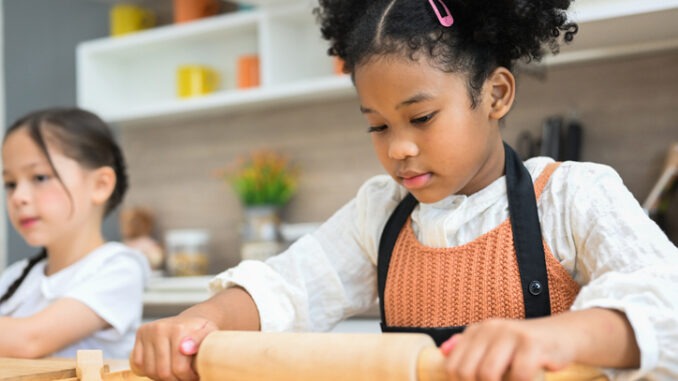 Happy children girls with bread and cookies playing with flour and laugh in kitchen, Little girls making bread in the kitchen, Children standing at cooking counter preparing ingredient for dinner meal