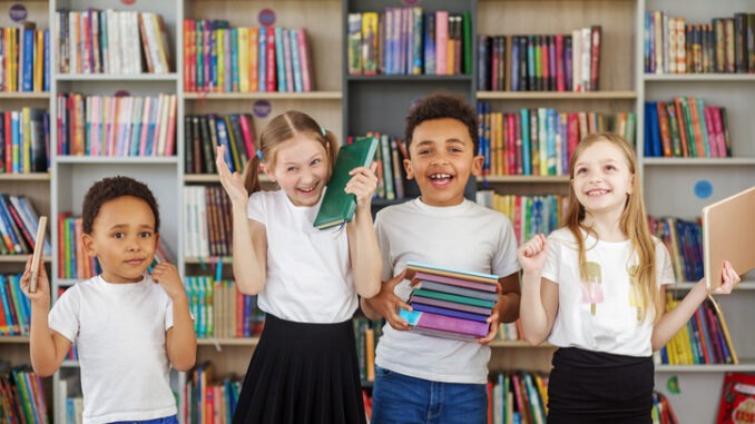 Four children holding stack of books in library. Multiethnic classmates having fun. World Book Day. Benefits of everyday reading.