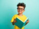 Photo of intelligent schoolboy with brown hair dressed yellow t-shirt holding book look empty space isolated on turquoise color background.