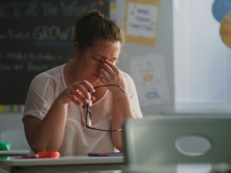 Tired Female Teacher Sitting Alone at the Desk in Empty Classroom, Relaxing After Class. Woman Feeling Stress, Burnout and Mental Exhaustion in Educational Environment, Working in Elementary School.
