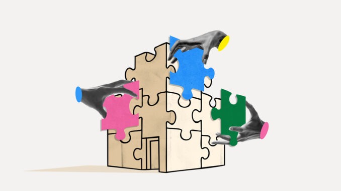 Several hands fit colorful puzzle pieces into the shape of a building on a light background. Concept of team collaboration, organizational development, integration and planning