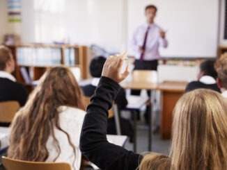 Female Student Raising Hand To Ask Question In Classroom
