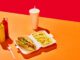 Tasty hotdog with sausage served mustard and ketchup with green salad with refreshing drinks and fried potato against vivid red background. Concept of fast food, street food, delivery. Copy space. Ad