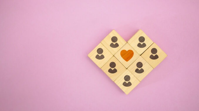 Wooden blocks forming people around a heart symbol, representing community, connection, love, and emotional support.
