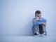 Young boy with hypersensitivity sitting alone on the floor against the wall with copy space