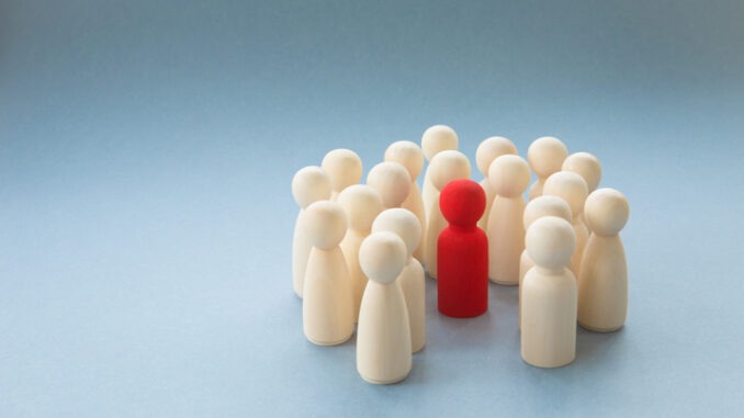 A socially diverse person being surrounded and protected by a crowd of people for being different. Alternatively a Manager or boss at a pep rally being surrounded by workers and team mates
