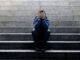 Young desperate man in casual clothes abandoned lost in depression sitting on ground street concrete stairs alone suffering emotional pain, sadness, looking sick in grunge lighting
